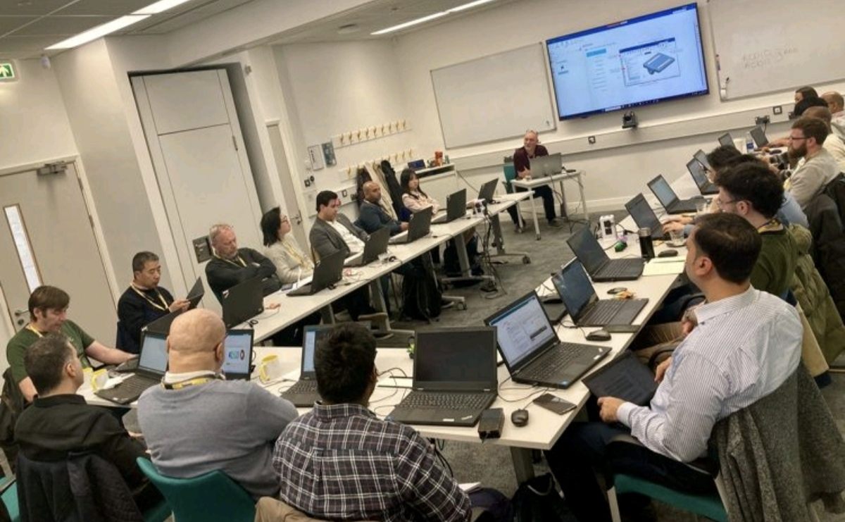 Academic workshop discussion with laptops and presentation screens.